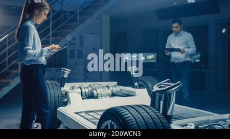 Team of Automotive Engineers Working on Electric Car Chassis Platform, Taking Measures, working with 3D CAD Software, Analysing Efficiency. Vehicle Stock Photo