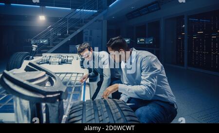 Two Automotive Engineers Working on Electric Car Chassis Platform, Taking Measures, working with 3D CAD Software, Analysing Efficiency. Vehicle Frame Stock Photo