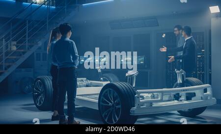 Automobile Engineers Discussing and Designing Electric Car Chassis Platform, Using Tablet Computers with 3D CAD Software. In Automotive Innovation Stock Photo