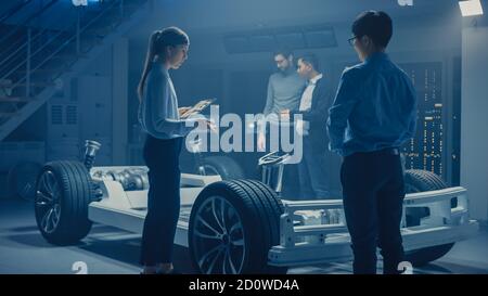 Automobile Engineers Discussing and Designing Electric Car Chassis Platform, Using Tablet Computers with 3D CAD Software. In Automotive Innovation Stock Photo