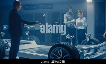Automobile Engineers Discussing and Designing Electric Car Chassis Platform, Using Tablet Computers with 3D CAD Software. In Automotive Innovation Stock Photo