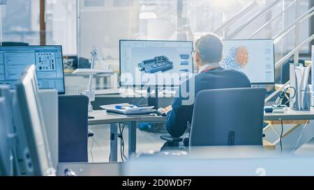 Back View of Industrial Engineer Working on Desktop Computer in Bright Office. Screens Show IDE / CAD Software, Implementation of Machine Learning Stock Photo