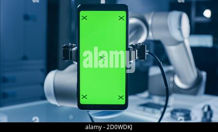 Real Robot Arm Holding Green Mock-Up Screen Smartphone Device. Industrial Robotic Manipulator End Effector Holds Mobile Phone with Chroma Key Display Stock Photo