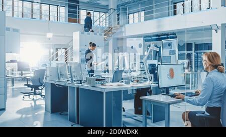 Diverse Team of Engineers Working on Computers, Program and Manipulate Robot Arm, Discuss Problems in Bright Industrial Robotics Technology and Design Stock Photo