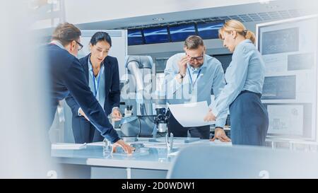 Diverse Team of Industrial Robotics Engineers Uses Tablet Computer to Program and Manipulate Robot Arm for Lifting, Moving Objects. Technology Stock Photo
