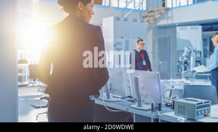 Shot of Stylish Female Engineer Enters Bright Modern Research Facility and Joins Team of other Robot and IT Specialists Stock Photo