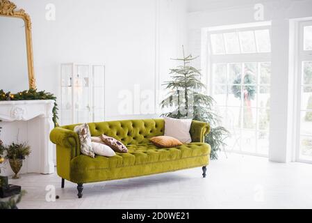 The green velour sofa with pillows in the bright attic room has an artificial fireplace.A spacious living room with white walls and a decorated Christ Stock Photo