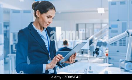 Stylish Female Industrial Robotics Engineer Uses Tablet Computer to Program and Manipulate Robot Arm for Lifting, Moving Objects. Technology Research Stock Photo