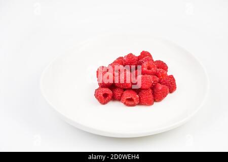 Raspberries on a white plate on a light background. Berry background. Stock Photo