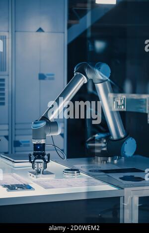 Vertical Shot of Futuristic Artificial Intelligence Robotic Arm Operates and Moves a Metal Object, Picks It Up and Puts it Down. Scene is Taken in a Stock Photo