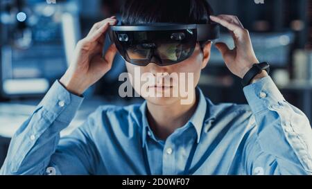 Professional Japanese Electronics Development Engineer in Blue Shirt is Wearing a Virtual Reality Headset and Looking Around the High Tech Research Stock Photo