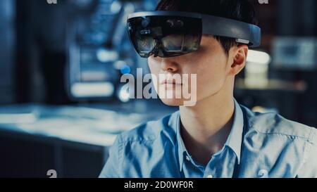 Professional Japanese Electronics Development Engineer in Blue Shirt is Wearing a Virtual Reality Headset and Looking Around the High Tech Research Stock Photo