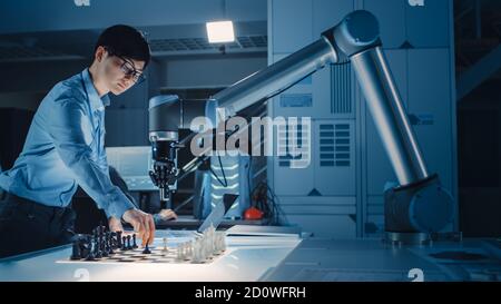 Professional Japanese Development Engineer is Testing an Artificial Intelligence Interface by Playing Chess with a Futuristic Robotic Arm. They are in Stock Photo