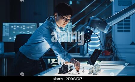 Professional Japanese Development Engineer is Testing an Artificial Intelligence Interface by Playing Chess with a Futuristic Robotic Arm. They are in Stock Photo