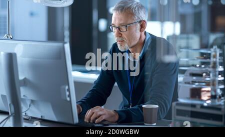 Middle Aged Electronics Repair Engineer Working on Personal Computer in His Workshop, Checks Motherboard. In the Background Various Circuit Boards Stock Photo