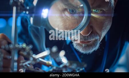 Electronics Maintenance and Repair Engineer Soldering Motherboard, Microchip and Circuit Board, Looking through Magnifying Glass. Conceptual Shot Stock Photo