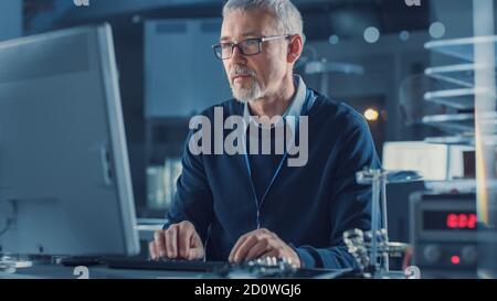 Middle Aged Electronics Repair Engineer Working on Personal Computer in His Workshop, Checks Motherboard. In the Background Various Circuit Boards Stock Photo