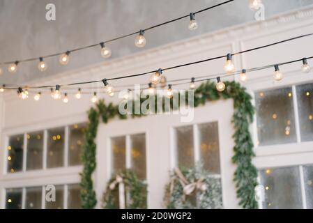 A retro garland of incandescent lamps is lit against the background of the entrance doors to the house, decorated with Christmas wreaths Stock Photo