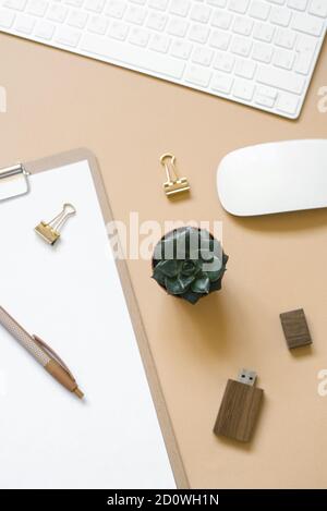 A tablet with a clean sheet of paper is on a beige background, a table with a computer and supplies. Top view and copy space Stock Photo