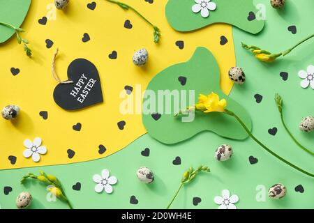 Easter background in green and yellow. Flat lay, top view with quail eggs, freesia flowers and black heart confetti. Stock Photo