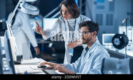 Machine Engine Development Engineer Working on Computer at His Desk, Talks with Female Project Manager. Team of Professionals Working in the Modern Stock Photo