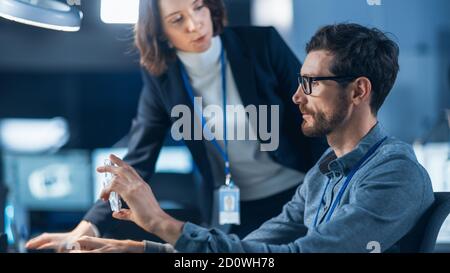 Futuristic Machine Engine Development Engineer Working on Computer at His Desk, Talks with Female Project Manager. Team of Professionals Working in Stock Photo