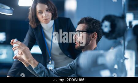 Futuristic Machine Engine Development Engineer Working on Computer at His Desk, Talks with Female Project Manager. Team of Professionals Working in Stock Photo