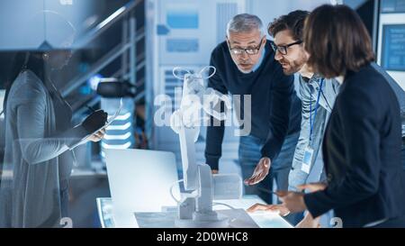 Engineers Meeting in Robotic Research Laboratory: Engineers, Scientists and Developers Gathered Around Illuminated Conference Table, Talking, Using Stock Photo