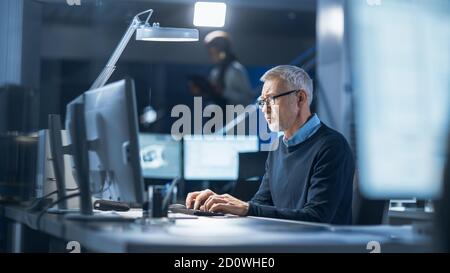 Shot of Industrial Engineer Working in Research Laboratory Development Center, Using Computer. In the Background Technology Development Laboratory Stock Photo