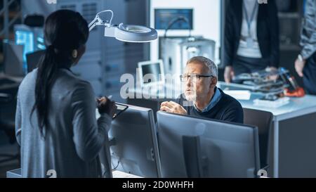 Shot of Male Industrial Engineer Talking with Female Manager about New Efficient Engine Concept Design. Diverse International Team of Industrial Stock Photo