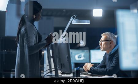 Shot of Male Industrial Engineer Talking with Female Manager about New Efficient Engine Concept Design. Diverse International Team of Industrial Stock Photo