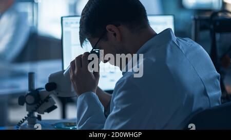 Shot of a Male IT Scientist Uses Computer with Electronic Microscope. In the Background Technology Development Laboratory with Scientists, Engineers Stock Photo