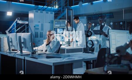 Diverse International Team of Industrial Scientists and Engineers Wearing White Coats Working on Industrial Machinery Design in Research Laboratory Stock Photo