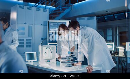 Diverse International Team of Industrial Scientists and Engineers Wearing White Coats Working on Heavy Machinery Design in Research Laboratory Stock Photo