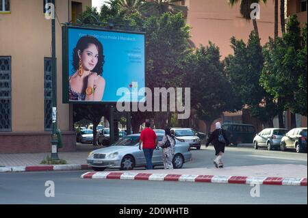 Traditionally dressed women with headscarves pass a billboard with a scantily clad fashion model on a billboard in a street in Marrakech, Morocco Stock Photo