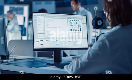 Over the Shoulder Shot: Female IT Scientist Uses Computer Showing System Monitoring and Controlling Program. In the Background Technology Development Stock Photo