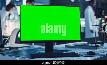 On the Desk Standing Green Mock-up Screen Computer. In the Background Technology Development Laboratory with Scientists, Engineers Working on High Stock Photo
