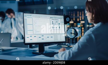 Over the Shoulder Shot: Female IT Scientist Uses Computer Showing System Monitoring and Controlling Program. In the Background Technology Development Stock Photo