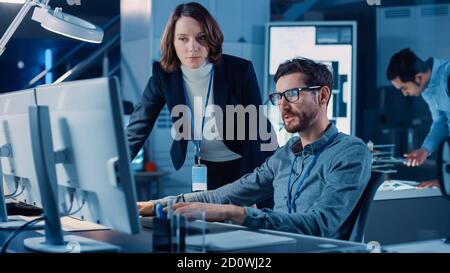 Futuristic Machine Engine Development Engineer Working on Computer at His Desk, Talks with Female Project Manager. Team of Professionals Working in Stock Photo