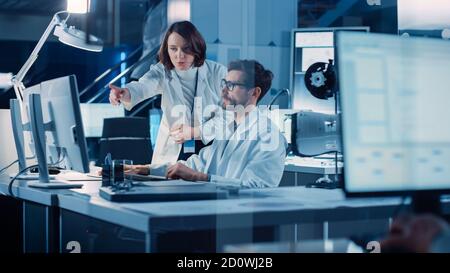 Machine Engine Development Engineer Working on Computer at His Desk, Talks with Project Manager, Shows Prototype Component. Team of Professionals Stock Photo