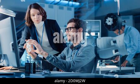 Futuristic Machine Engine Development Engineer Working on Computer at His Desk, Talks with Female Project Manager. Team of Professionals Working in Stock Photo