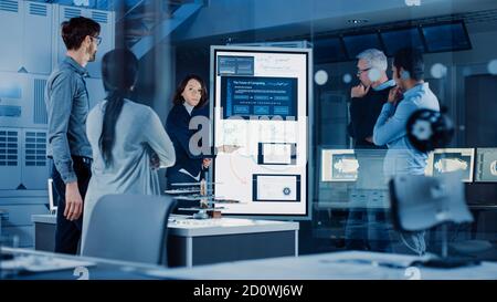 Engineers Meeting in Technology Research Laboratory: Female Engineer Leads Presentation Writes on Interactive Digital Whiteboard, Shows Machine Stock Photo