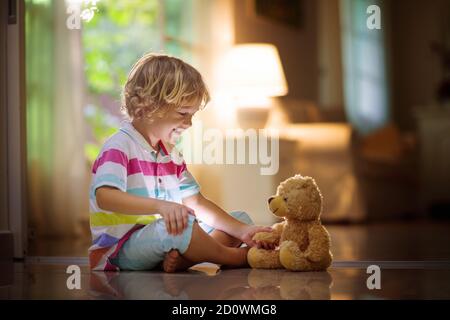 Child playing with teddy bear. Little boy hugging his favorite toy. Kid and stuffed animal at home. Toddler sitting on the floor of living room with b Stock Photo