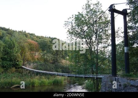 A serene suspension bridge in the middle of the forest over a river Stock Photo