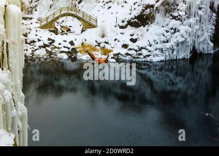 A diver jumps from a cliff into a volcanically heated pool in the middle of winter. Stock Photo