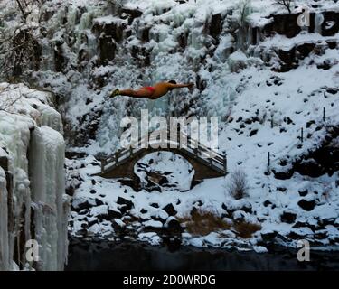 A diver jumps from a cliff into a volcanically heated pool in the middle of winter. Stock Photo