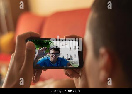 selective focus videoconference of two young people made by the mobile one lying on the couch at home and another young man in the middle of nature in Stock Photo