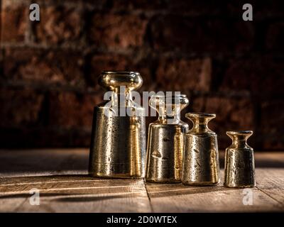 Vintage 1800's Brass and Lead weights set of 4 pitted and weathered on timber flooring with brick background Stock Photo