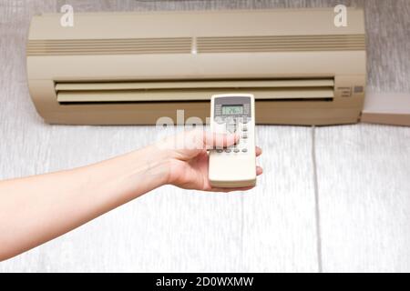 The woman turns on the household split system using the remote control. Stock Photo