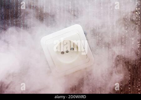 Smoke appeared from a faulty electrical outlet due to a short circuit in the electrical wiring. Stock Photo